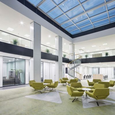 A large commercial area with several small tables and chairs and a glass roof.